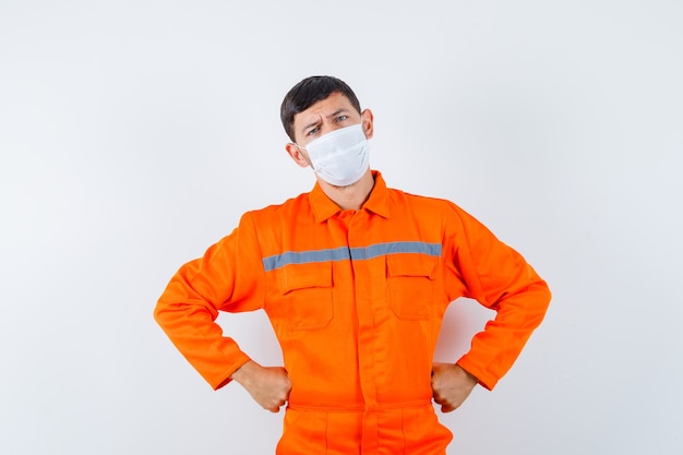 Foto gratuita hombre industrial cogidos de la mano en la cintura en uniforme, máscara y mirando pensativo. vista frontal.