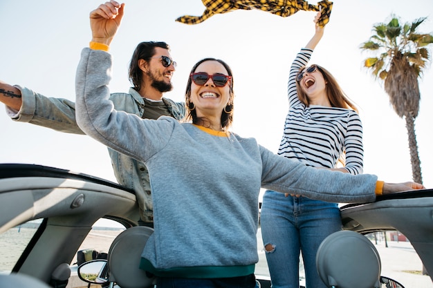 Foto gratuita hombre positivo y mujeres sonrientes divirtiéndose e inclinándose fuera del auto
