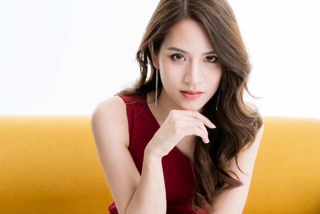 Foto gratuita hermosa mujer asiática de elegancia atractiva en vestido rojo sentarse y relajarse pose de modelo en sesión de fotos de estudio de sofá amarillo
