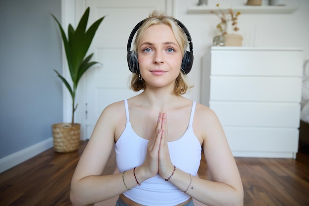 Foto gratuita imagen de una mujer joven escuchando un podcast de yoga para principiantes sosteniendo las manos en un signo de namaste