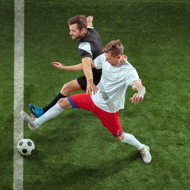 Foto gratuita jugador de fútbol que aborda la pelota sobre la pared de hierba verde. jugadores de fútbol masculino profesional en movimiento en el estadio. montar hombres saltadores en acción, salto, movimiento en el juego.