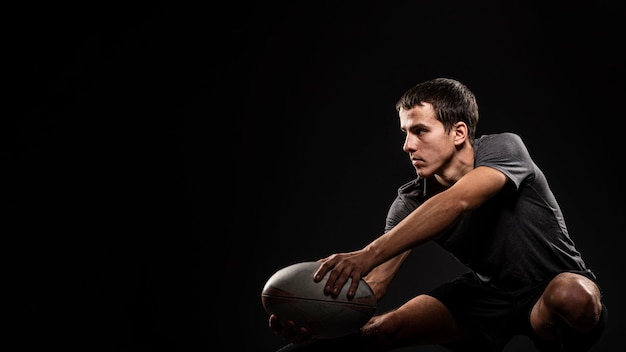 Jugador de rugby masculino atlético hermoso que sostiene la bola con el espacio de la copia