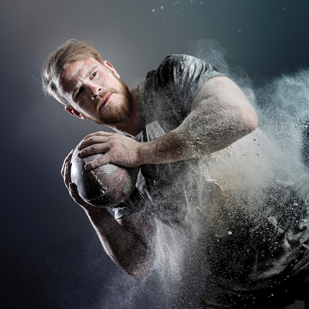 Jugador de rugby masculino atlético sosteniendo la bola con polvo