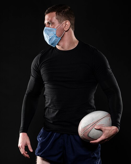Jugador de rugby masculino con máscara médica y pelota