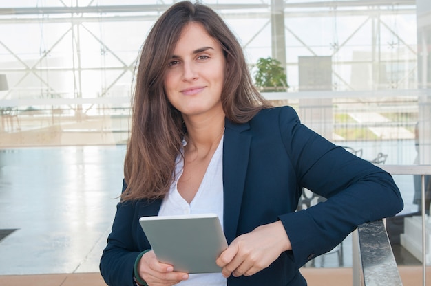 Foto gratuita mujer en la oficina mirando a cámara, sosteniendo la tableta en las manos