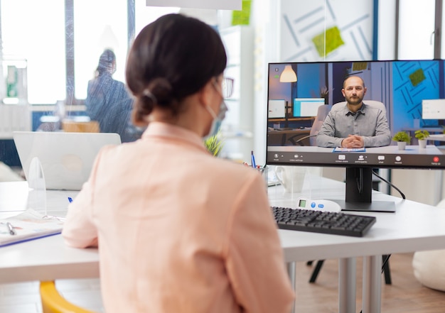 Foto gratuita mujer en la nueva oficina normal escuchando a un hombre hablando durante una videoconferencia en línea, mirando la pantalla discutiendo el proyecto durante el brote de gripe por coronavirus.