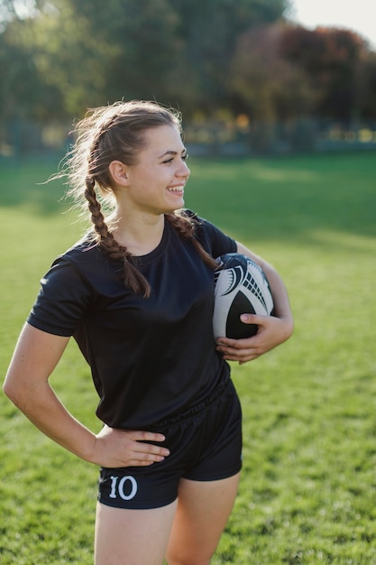 Foto gratuita mujer sosteniendo una pelota de rugby y mirando a otro lado