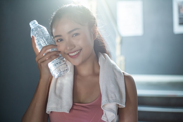 Foto gratuita mujer de pie y relajante después de hacer ejercicio, sosteniendo una botella de agua para tocar la cara.