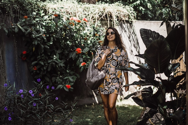 niña con una mochila, con gafas de sol, en un jardín tropical