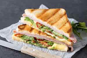 Foto gratuita sándwich de panini con jamón, queso, tomate y rúcula sobre fondo de pizarra negra