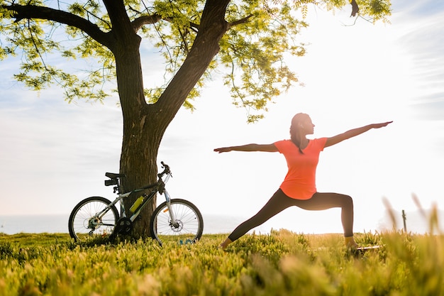 Foto gratuita silueta de mujer hermosa delgada haciendo deporte en la mañana en el parque haciendo yoga