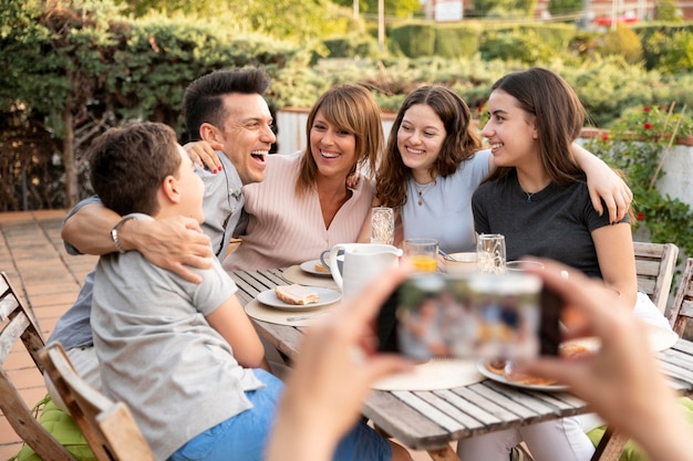 Foto gratuita persona con smartphone tomando fotos de la familia almorzando juntos al aire libre