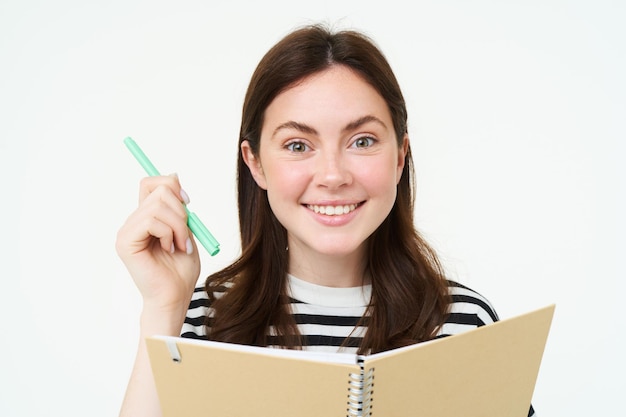 Foto gratuita retrato de una chica creativa sonriente escribiendo memos en un planificador sosteniendo un bolígrafo y un cuaderno hace notas