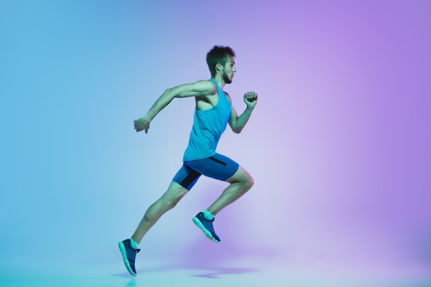 Foto gratuita retrato de cuerpo entero de un hombre joven activo corriendo, caucásico, corriendo en estudio de gradiente en luz de neón