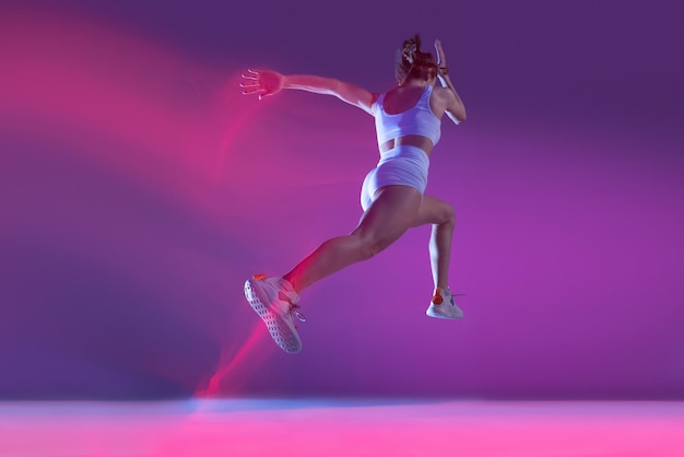 Foto gratuita retrato dinámico de una joven deportista entrenando corriendo aislada sobre un fondo morado en neón con luces mixtas