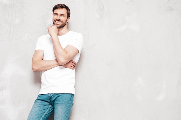 Foto gratuita retrato de guapo sonriente con estilo hipster lambersexual modelo sexy hombre vestido con camiseta y jeans moda hombre aislado en la pared azul en el estudio