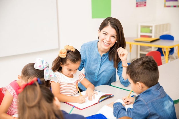 Foto gratuita retrato de una hermosa maestra de preescolar hispana enseñando a sus alumnos en un salón de clases