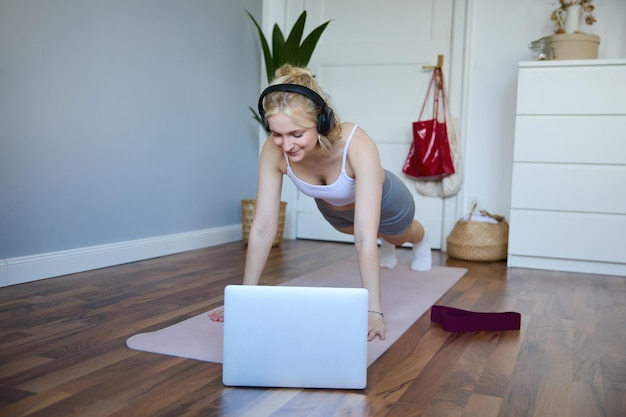 Foto gratuita retrato de una mujer joven y deportiva haciendo ejercicio mirando un video de fitness en una computadora portátil inalámbrica