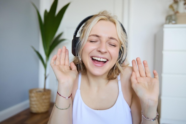 Foto gratuita retrato en primer plano de una joven sincera y feliz con auriculares cantando y escuchando música en casa