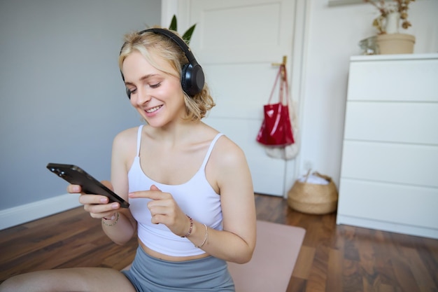 Foto gratuita retrato en primer plano de una joven rubia eligiendo un podcast de fitness mirando su teléfono móvil comprobando