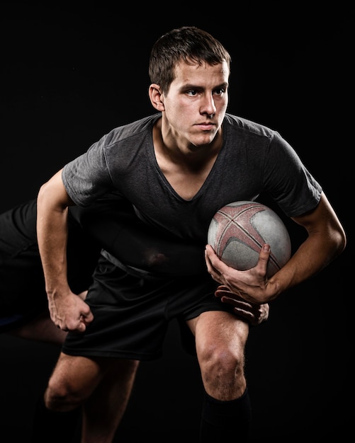 Vista frontal del jugador de rugby masculino sosteniendo la pelota con su brazo