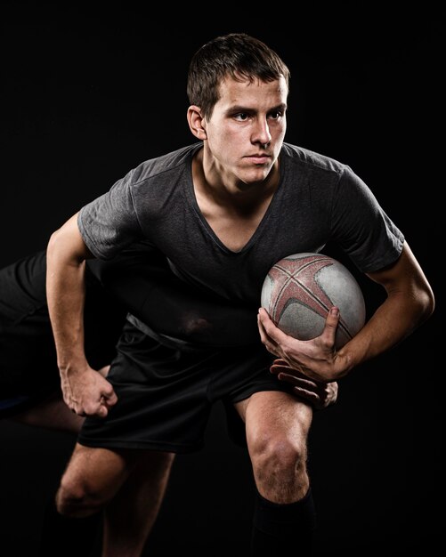 Vista frontal del jugador de rugby masculino sosteniendo la pelota con su brazo