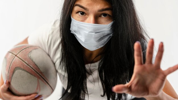 Vista frontal del jugador de rugby femenino con máscara médica y pelota
