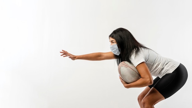 Vista lateral del jugador de rugby femenino con pelota y máscara médica