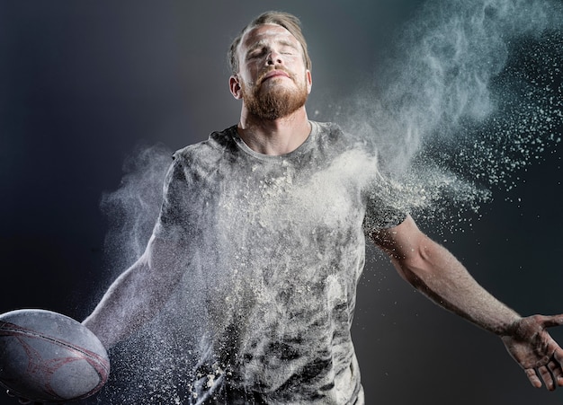 Giocatore di rugby maschile atletico che tiene palla con polvere