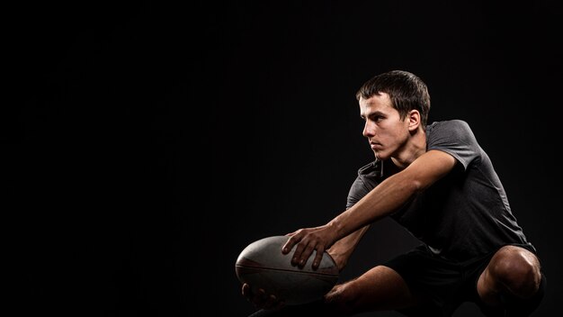 Giocatore di rugby maschio atletico bello che tiene palla con lo spazio della copia
