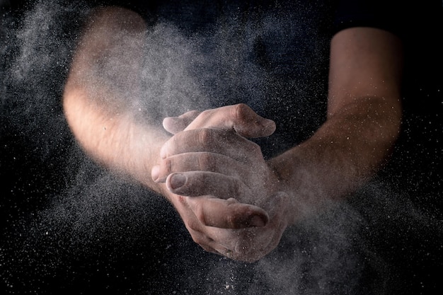 Un uomo batte le mani con farina sparsa su uno sfondo scuro Tema culinario