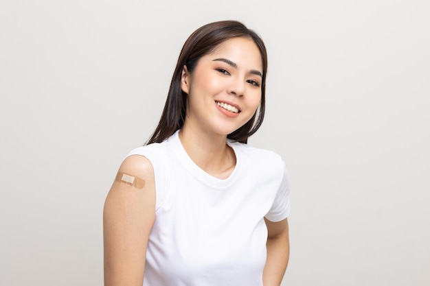 Vaccinazione. Giovane bella donna asiatica che ottiene un vaccino per proteggere il coronavirus. Femmina felice sorridente che mostra il braccio con la benda dopo aver ricevuto la vaccinazione. Su sfondo bianco isolato.