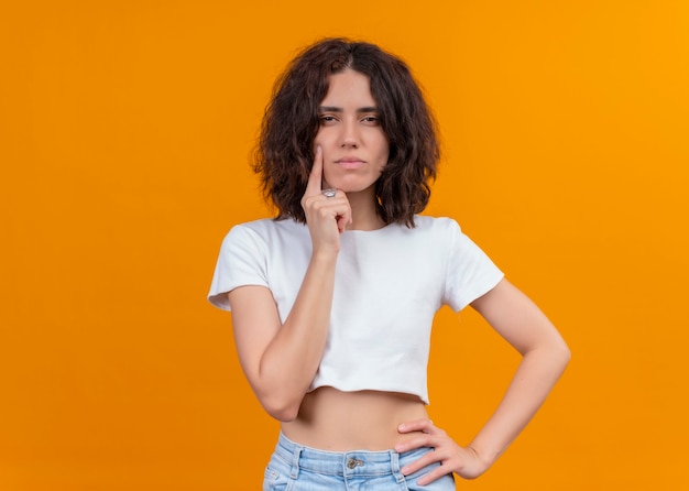 Free photo thoughtful young beautiful woman putting finger on cheek on isolated orange wall with copy space