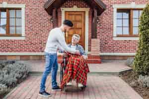 Бесплатное фото Сын помогает отцу на инвалидной коляске возле дома престарелых