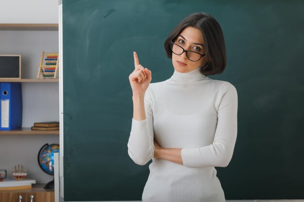 Бесплатное фото Мысли указывает на молодую учительницу в очках, стоящую перед доской в классе