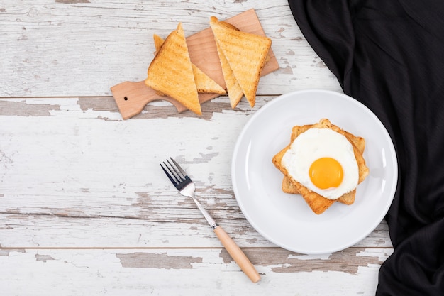 Взгляд сверху яичниц завтрака на белой плите с космосом тоста и экземпляра на деревянной поверхности горизонтальной