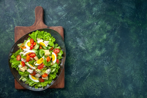 Free photo top view of delicious salad with many fresh ingredients on the right side on wooden cutting board on black green mix colors background