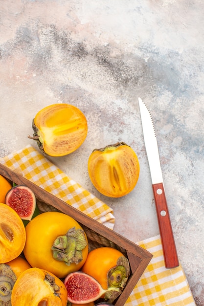 Free photo top view delicious persimmons and cut figs in wood box yellow kitchen towel a knife on nude background
