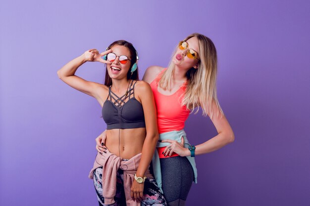 Two pretty girls in fashionable activewear posing on purpl