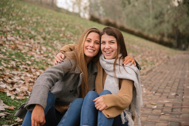 Бесплатное фото Две молодые женщины обнимаются и сидят в парке