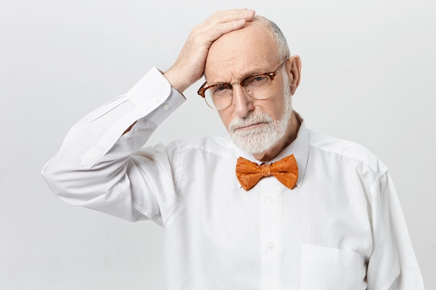 Free photo unhappy frustrated caucasian male pensioner with thick beard suffering from memory loss problem posing, rubbing his bald head, having depressed stressed facial expression, frowning