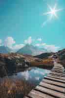 Бесплатное фото Вертикальный снимок деревянного прохода над небольшим озером и горным хребтом на горизонте.