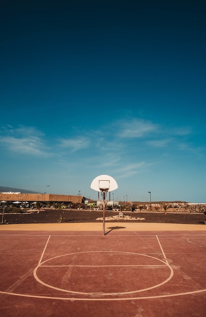 Foto gratuita colpo verticale di un campo da basket con il cerchio visibile sotto il cielo blu