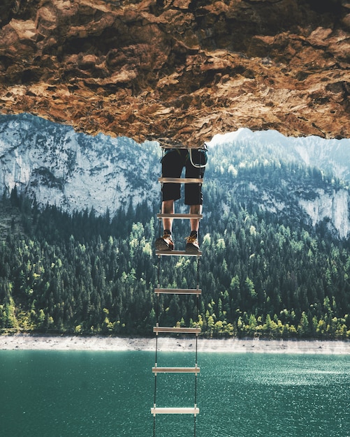 Free photo vertical shot of a person climbing up a ladder hanging from a cliff