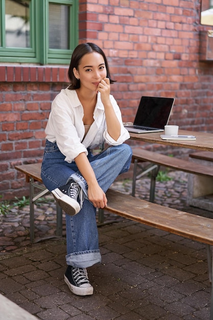Free photo vertical shot of trendy asian girl sitting in cafe alone with laptop working or studying browsing on