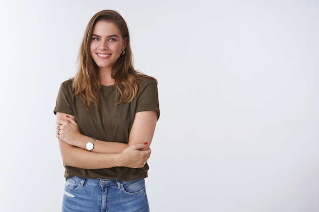 Free photo wellbeing people lifestyle concept. charming feminine tender outgoing young woman wearing olive t-shirt cross arms chest smiling cute flirty expressing positivity joyful attitude, white background