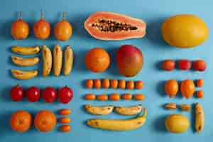 Free photo whole and slices of exotic fruits isolated on blue studio background. cumquat, bananas, red fortunella, yellow mango, lemons, peaches, physalis. creative summer composition. essential nutrition