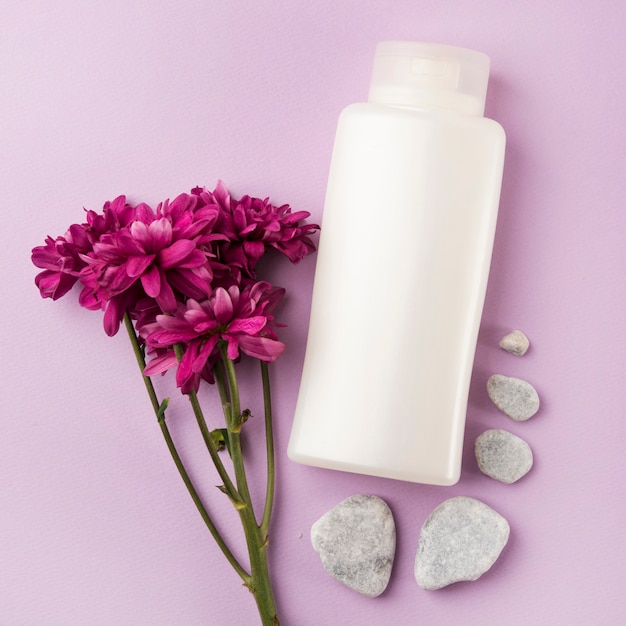 Free photo white cosmetics product with pink flower and spa stones on pink background