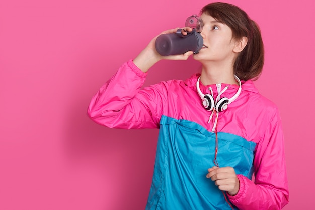 Бесплатное фото Женщина ношение синих и розовых спортивной питьевой воды из бутылки, модель позирует изолированные на розовый. молодой женский инструктор по фитнесу или личный тренер в студии.
