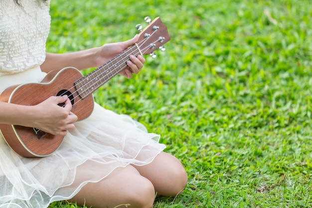 Женщина, одетая в милое белое платье и играющая на гавайской гитаре
